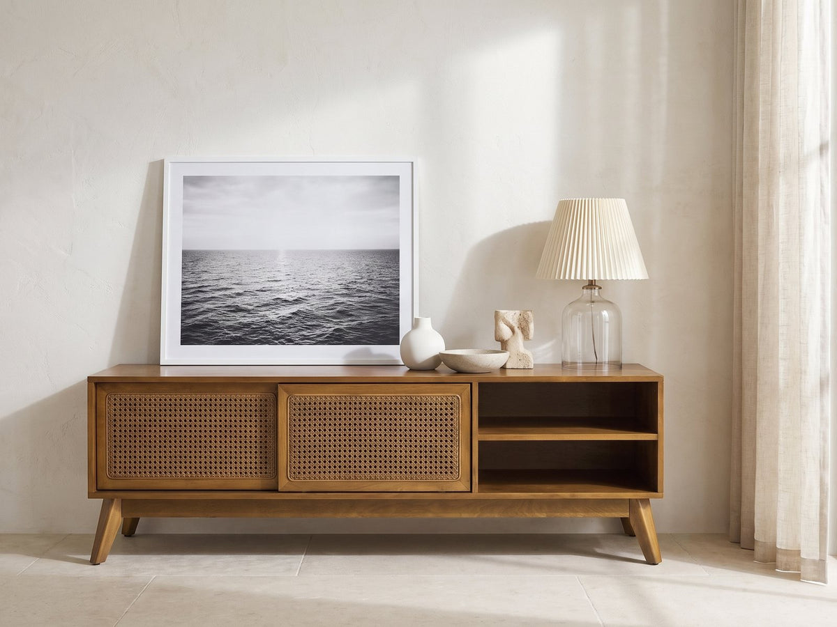 Cisternino 59-Inch Pecan Birch Veneer and Cane Media Console styled with a leaning print, a lamp and ceramics in a bright plaster room