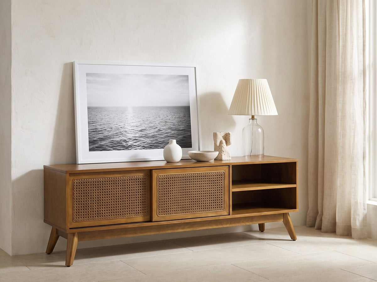 Cisternino 59-Inch Pecan Birch Veneer and Cane Media Console seen from the side, styled with a leaning print, a lamp and ceramics in a bright plaster room