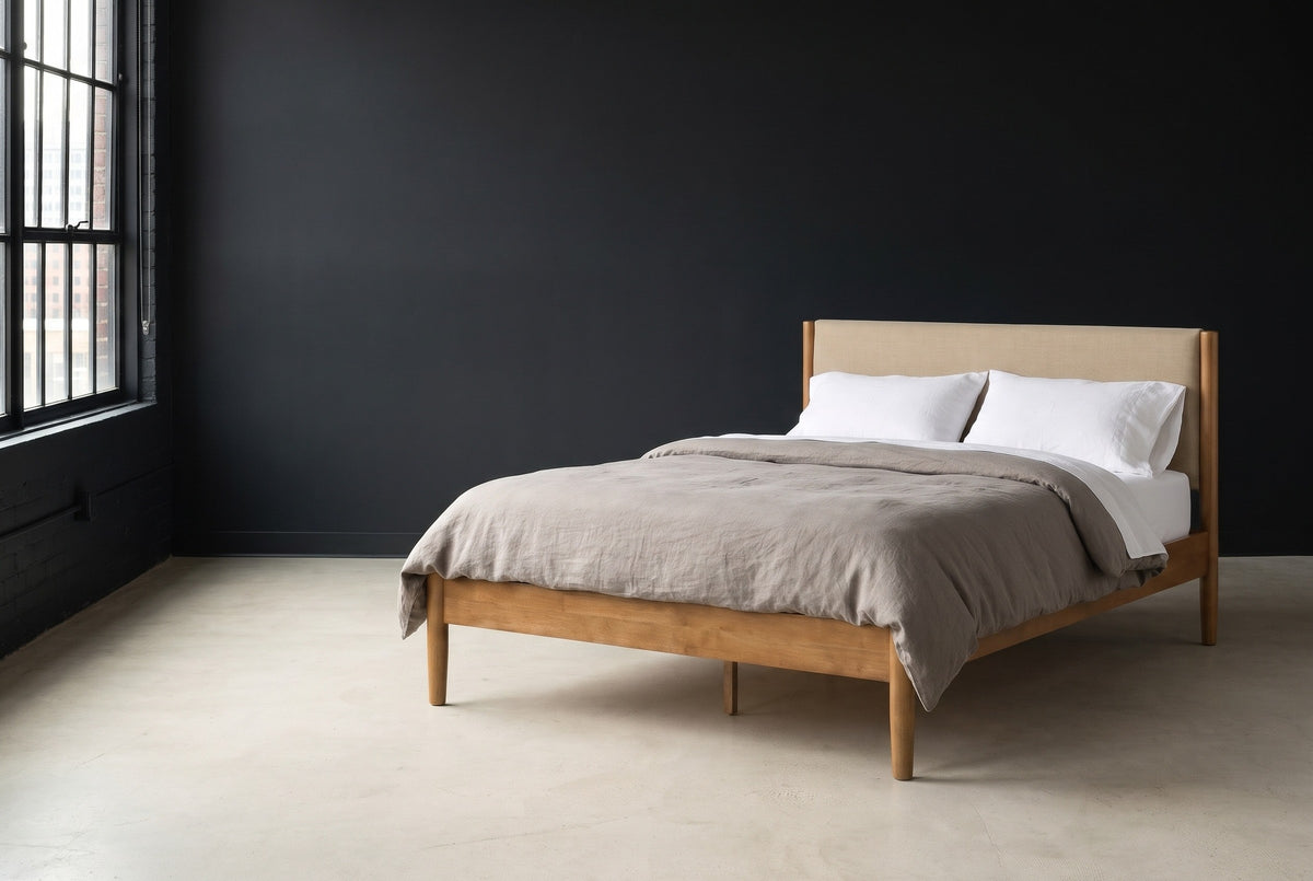 Civitella light walnut bed with a beige headboard against a charcoal wall in a Detroit loft, a tall black steel window at the left