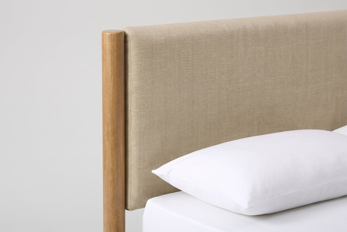 One side of the Civitella headboard: a round wooden post with a flat top beside the padded beige panel, above a white pillow