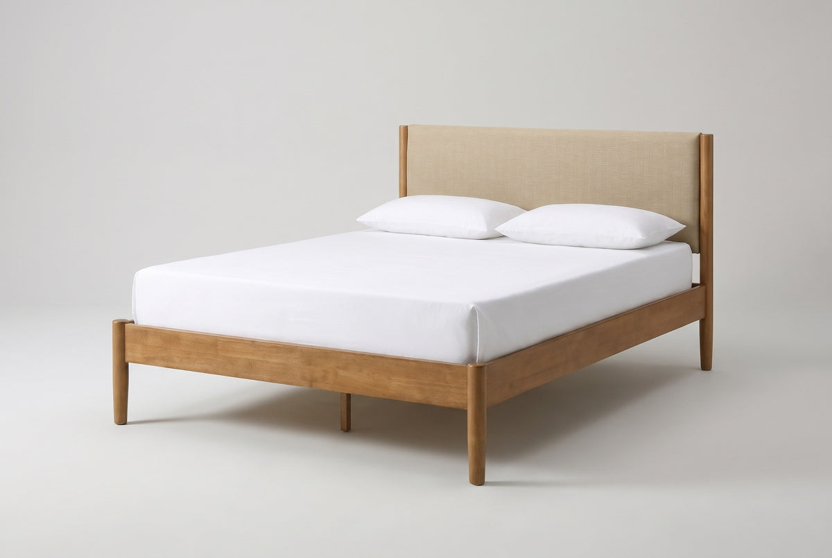 The Civitella bed in light walnut rubberwood with a beige headboard, a white mattress and pillows (not included), three-quarter view on a light studio backdrop