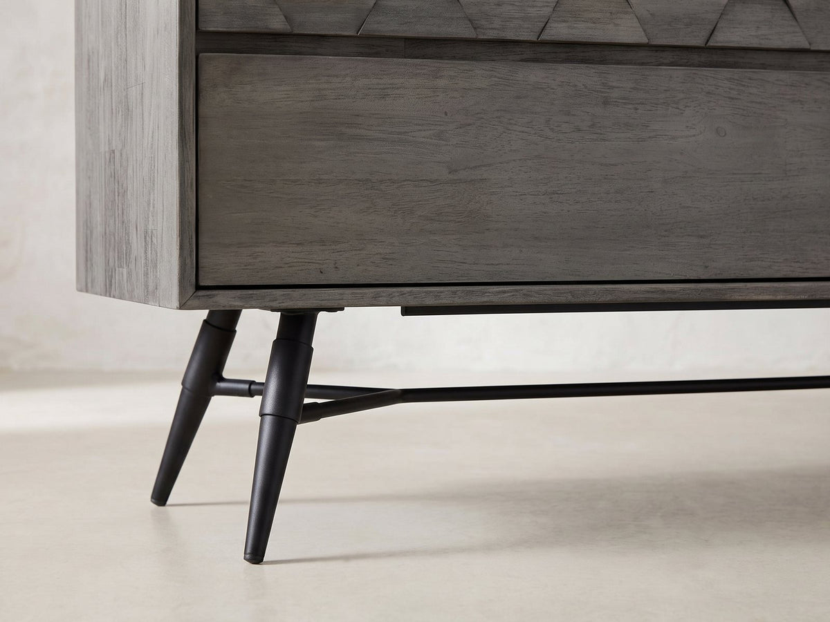 Close-up of the Codroipo 61-Inch Gray Acacia Honeycomb Dresser: the splayed black metal leg and stretcher rod
