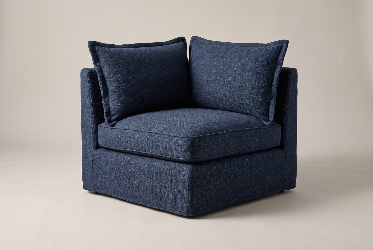 A single Comiso corner seat in navy slipcovers with two back pillows, on a light studio backdrop