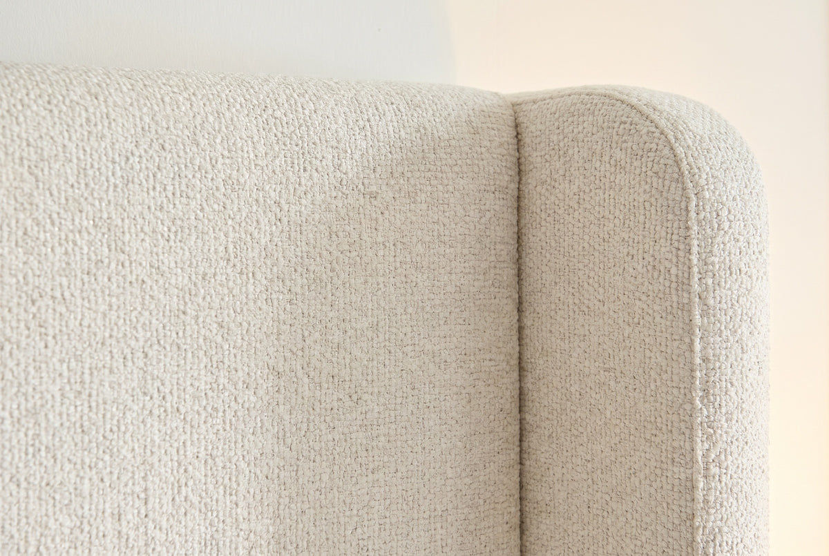 Close-up of the Conversano bed where the cream boucle wing meets the headboard panel along a plain seam