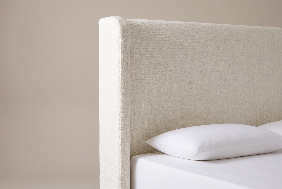 One side of the Conversano headboard: the cream boucle wing with a rounded top corner beside the plain flat panel, above a white pillow
