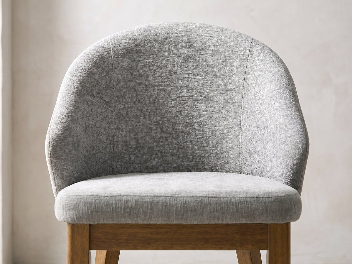 Close-up of the Crucoli 47-Inch Round Walnut-Finish Dining Set with 4 Chairs: the curved shell back and padded seat of a chair in light grey fabric