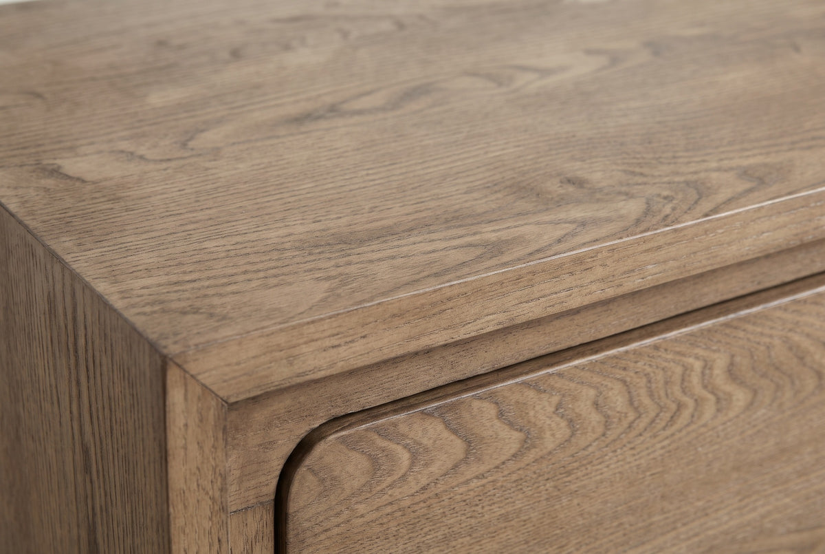 Close-up of the Cuglieri nightstand: latte elm veneer with open pores and a flowing grain, the mitred frame and the rounded corner of a drawer front