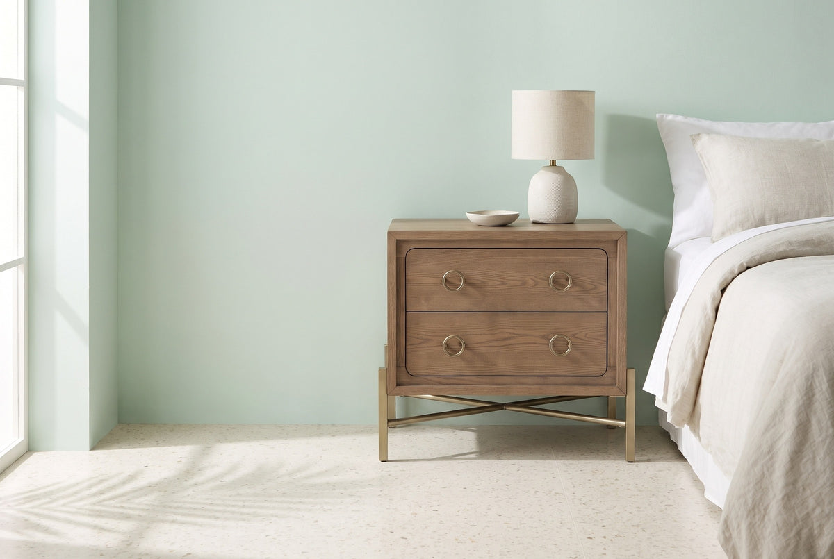 Cuglieri latte elm nightstand with brass-tone legs and a ceramic lamp beside a bed in a Miami bedroom with a pale mint plaster wall and a terrazzo floor