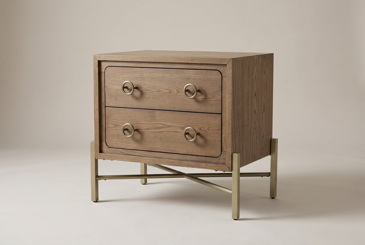 The Cuglieri two-drawer nightstand in latte elm with antique-brass ring pulls and a brass-tone metal X-base, three-quarter view on a light studio backdrop
