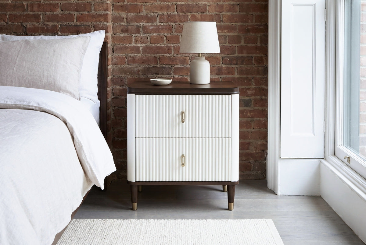 Desulo white fluted nightstand against an exposed red-brown brick wall in a Brooklyn brownstone bedroom with a tall sash window