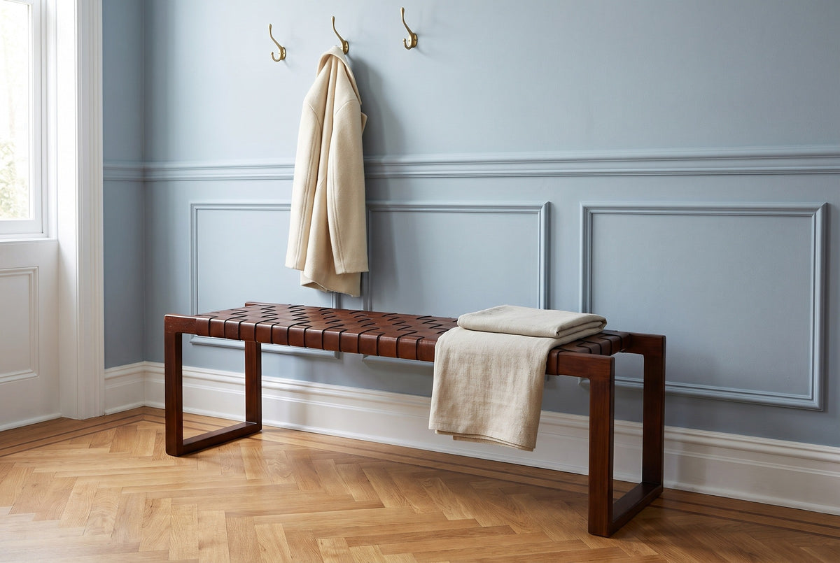 Fasano woven leather bench with a folded linen throw in a Philadelphia brownstone entry hall with a pale blue paneled wall, brass coat hooks and a herringbone oak floor