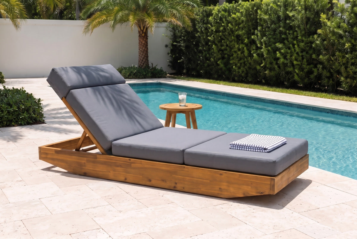 Ferla acacia chaise lounge with a dark grey cushion beside a lap pool in Boca Raton, Florida, with a white stucco wall, pale stone pavers and palms (side table and towel not included)