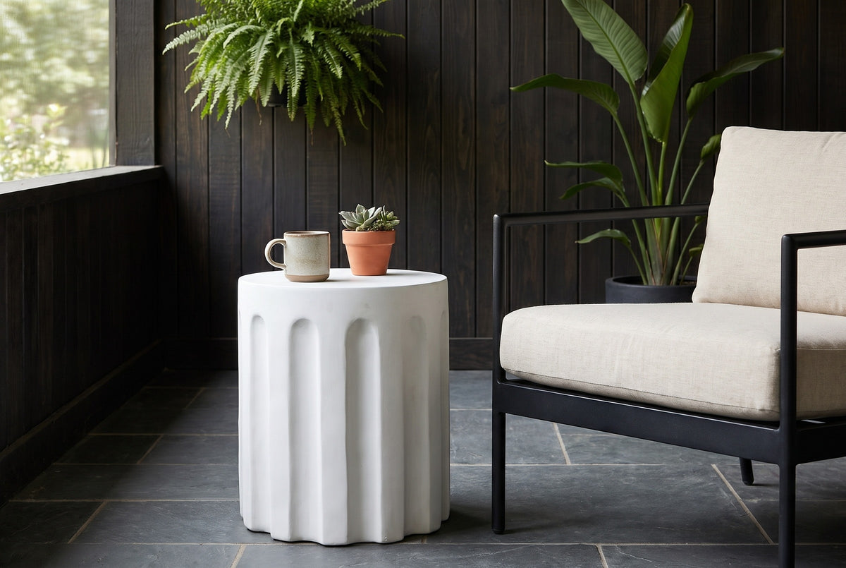 Ficuzza white fluted concrete side table with a stoneware mug and a small succulent beside a black lounge chair on a Fairhope, Alabama porch, dark cypress boards and charcoal slate tiles (chair and decor not included)
