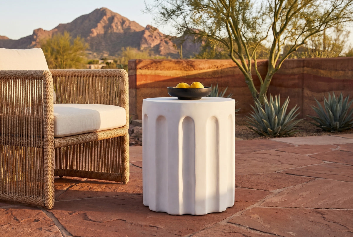 Ficuzza white fluted concrete side table with a black bowl of lemons beside a woven rope armchair on a red sandstone terrace in Paradise Valley, Arizona at golden hour, a rammed-earth wall, agaves and Camelback Mountain behind (chair and decor not included)