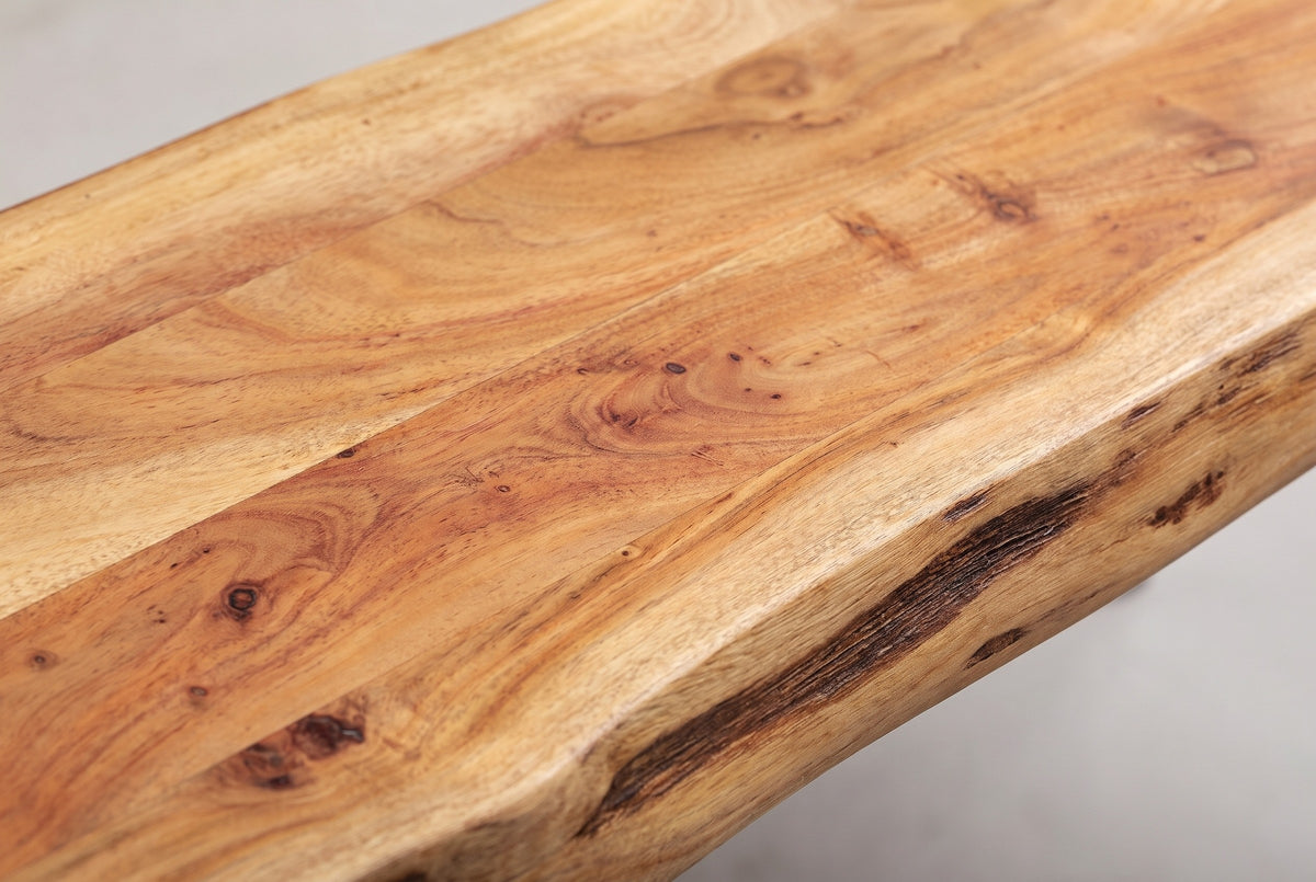 Close-up of the solid acacia top of the Foligno bench: honey and amber grain with small knots, board joints and a dark bark-coloured groove along the live edge