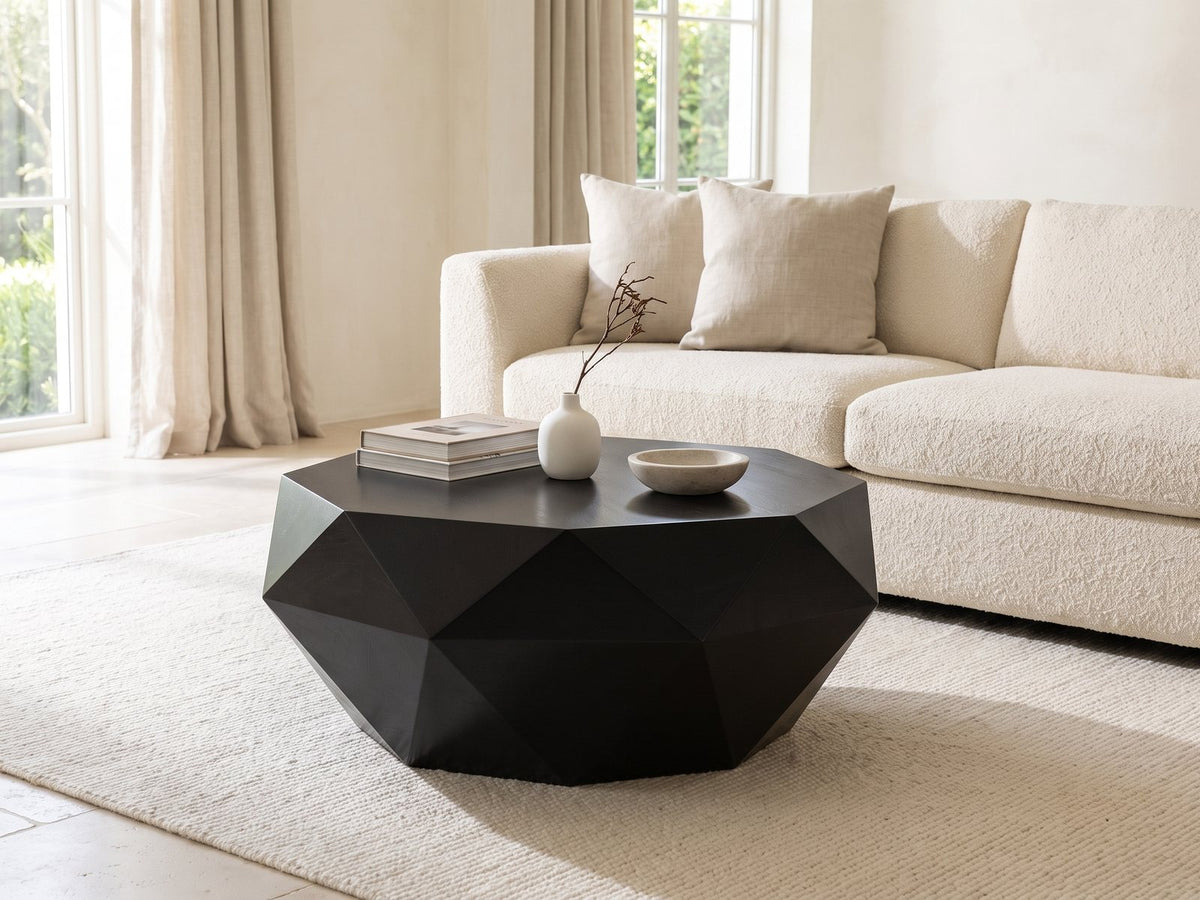 Follonica Faceted Acacia Coffee Table styled with books, a vase and a stone bowl in front of a cream sofa in a bright plaster room