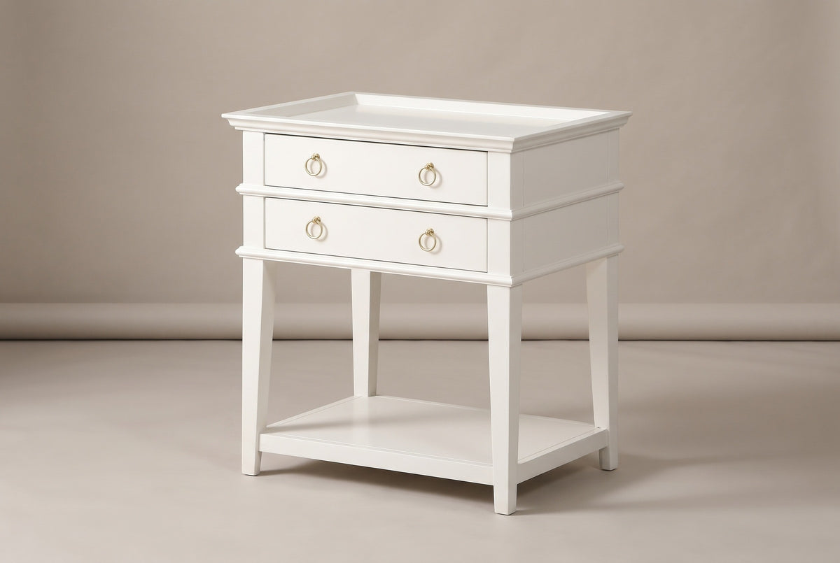 The Fonni two-drawer nightstand with a white tray top, two drawers with brushed gold ring pulls, moulded bands, square tapered legs and an open shelf, three-quarter view on a light studio backdrop