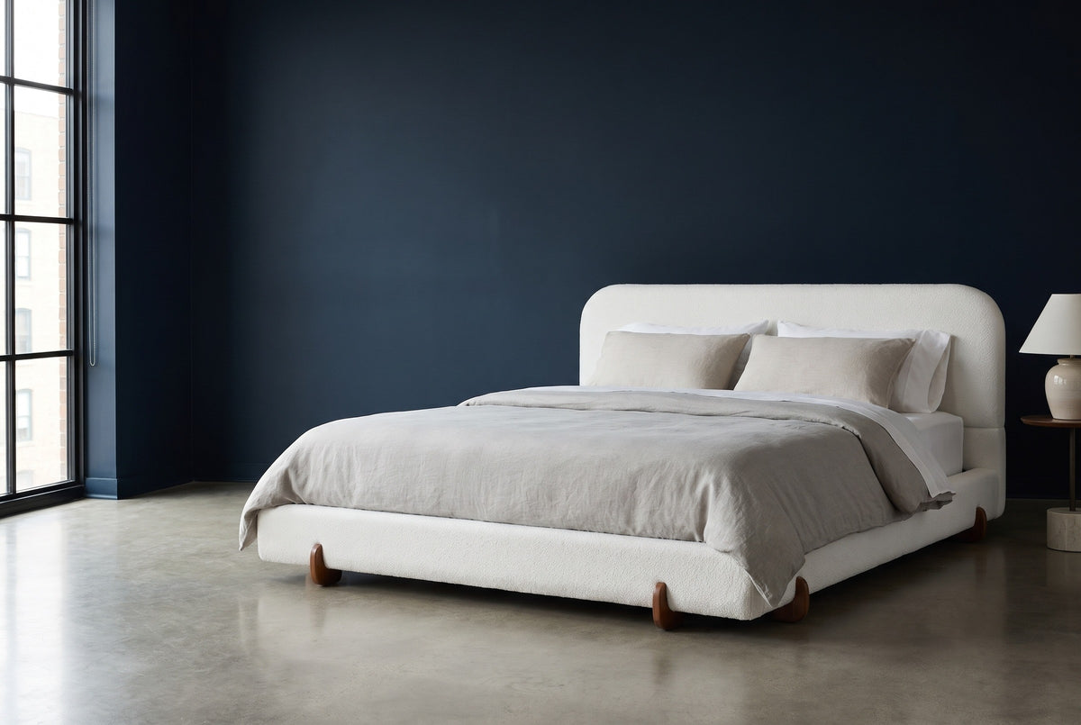 Fossacesia white textured fabric bed against a deep ink-navy wall in a Chicago loft, a tall black steel window at the left