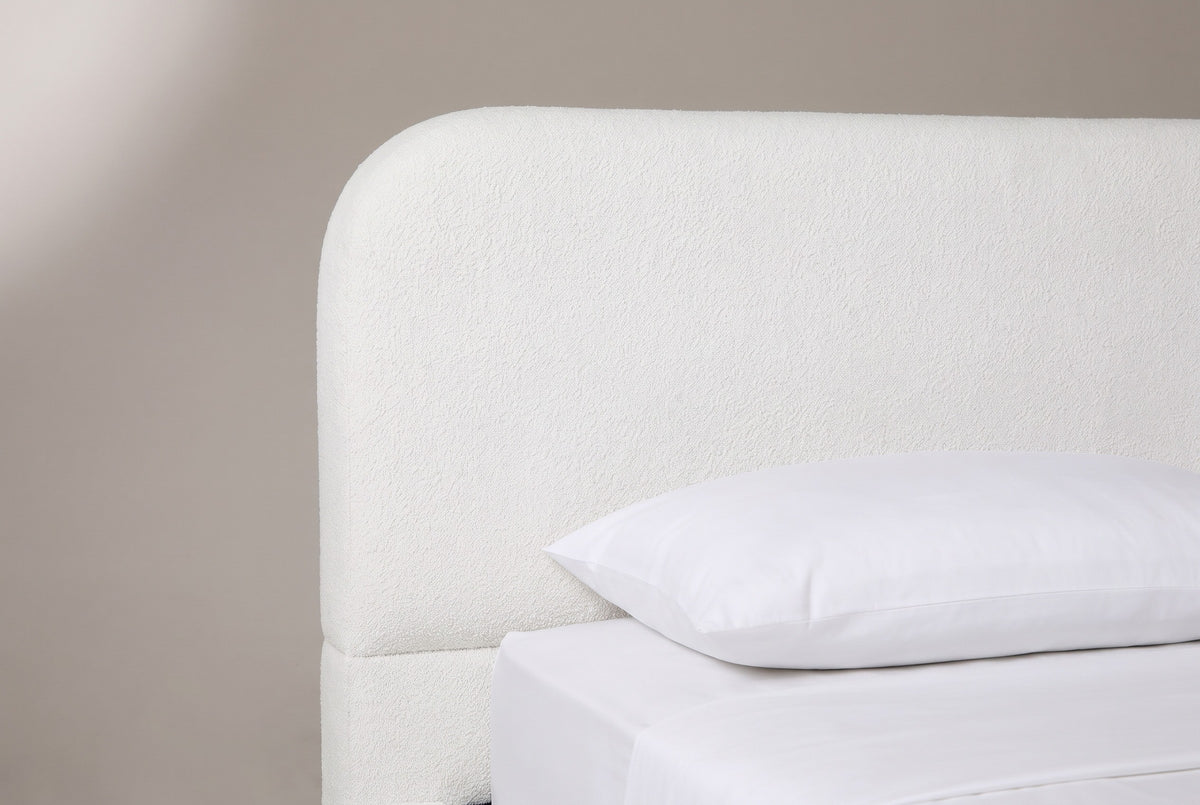 The upper corner of the Fossacesia headboard: a tall white textured panel with a large rounded top corner, a plain lower band and a white pillow