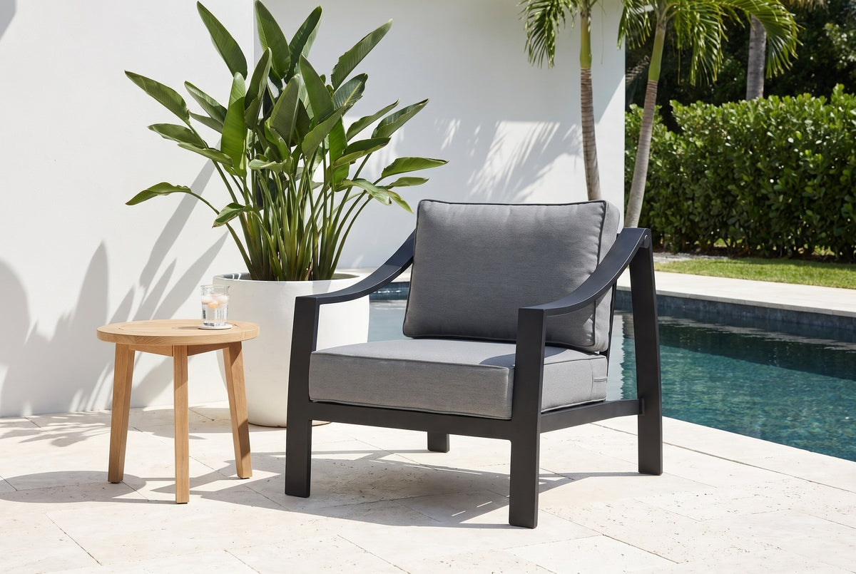 Galati black aluminum lounge chair on a travertine pool terrace in Naples, Florida, a white stucco wall, a bird of paradise and royal palms behind (side table not included)