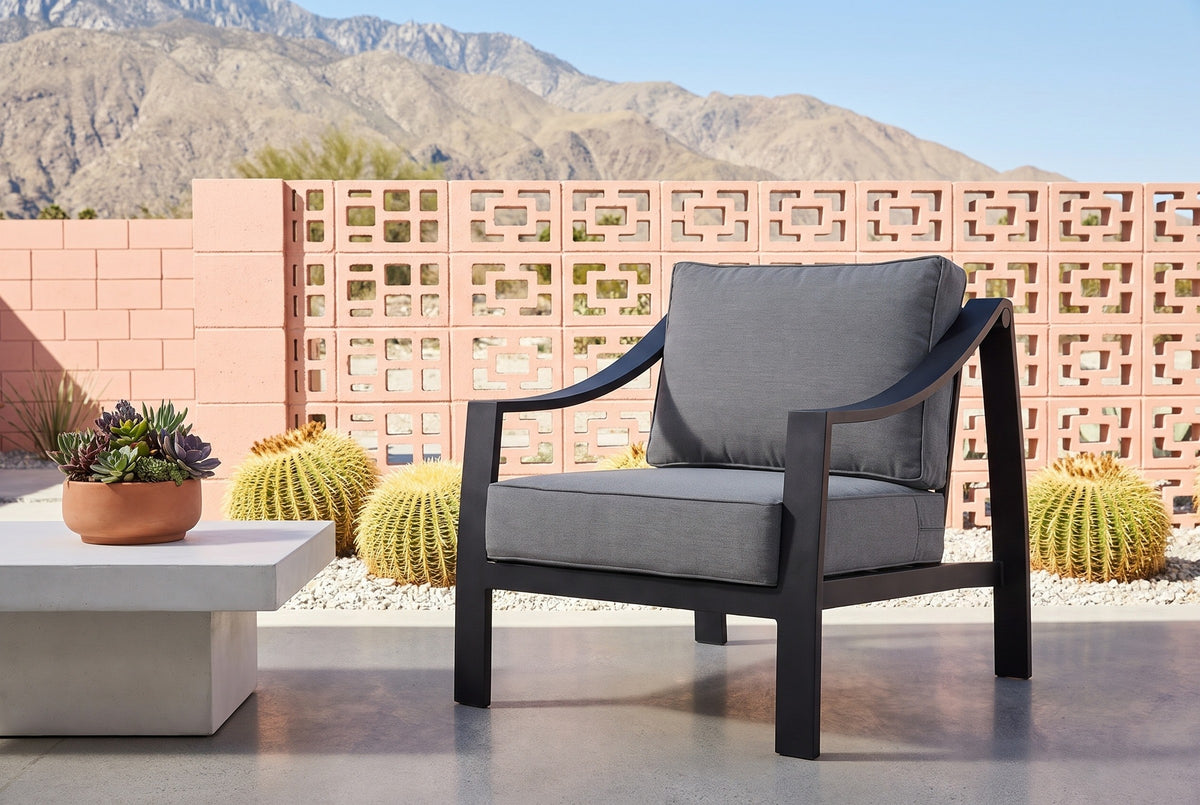 Galati black aluminum lounge chair on a polished concrete patio in Palm Springs, a coral-pink breeze-block wall, golden barrel cacti and mountains behind (table not included)