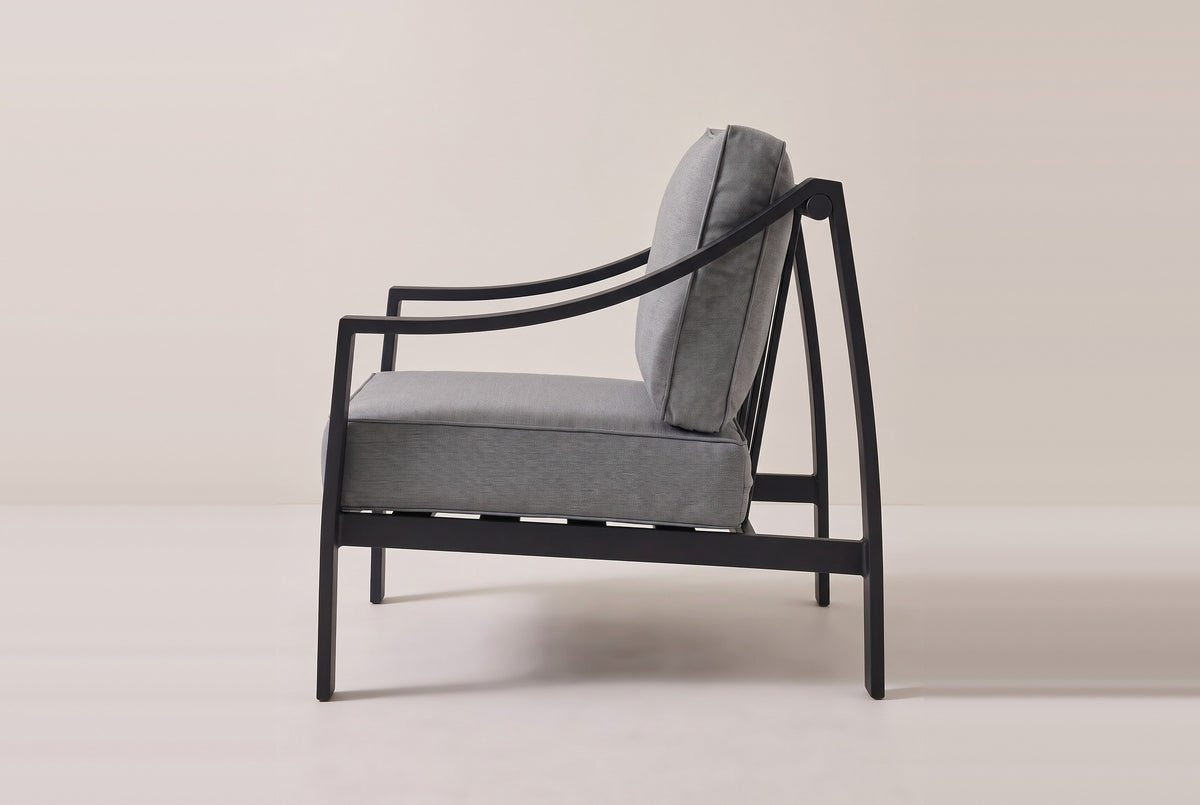 The Galati lounge chair seen from the side: the curved arm rising from the front leg to the round cap on the rear leg, the bowed rear leg and the side rail