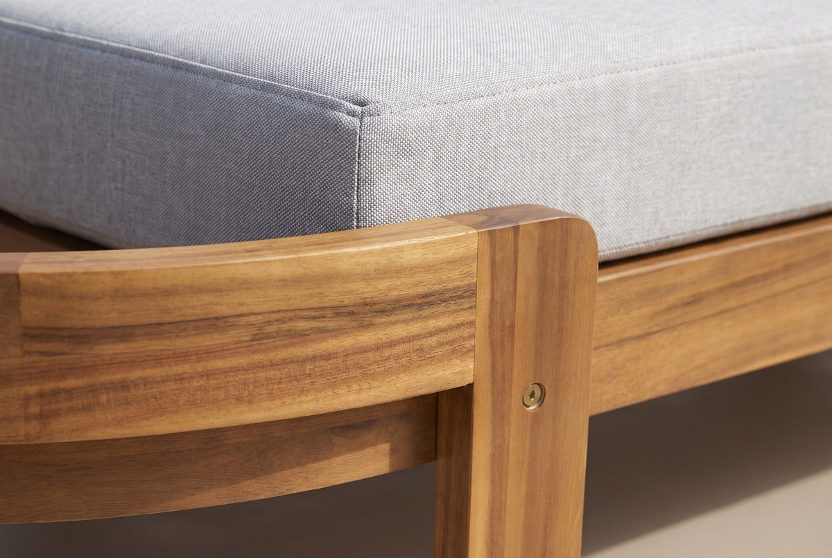Close-up of the solid acacia on the Gangi chaise: the curved head band and a square leg in teak finish with a bolt head, beside the light grey cushion