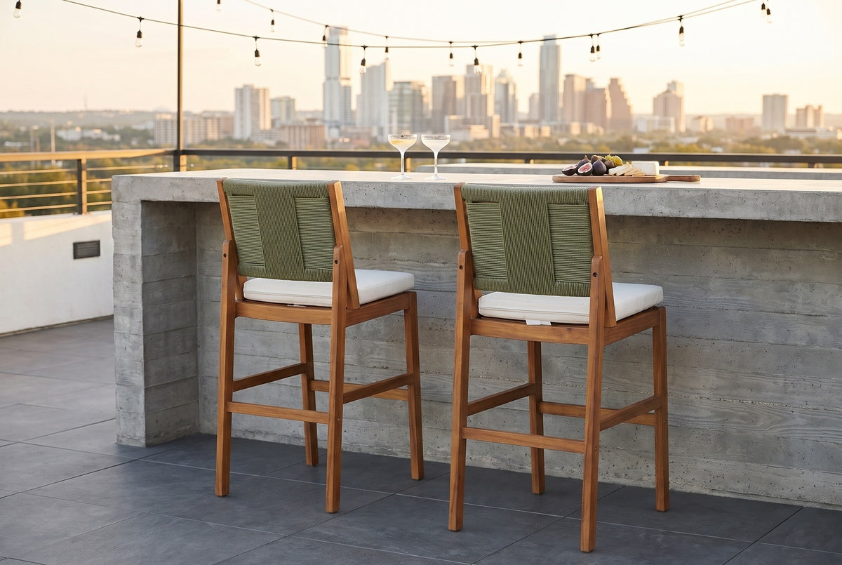 Two Ganzirri acacia bar stools tucked at a board-formed concrete bar on an Austin rooftop terrace at golden hour, string lights and the skyline behind (bar counter not included)
