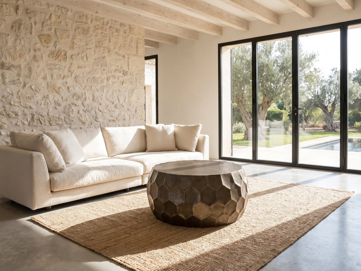 Gavi 32-Inch Round Antique Bronze Faceted Aluminum Drum Coffee Table on a jute rug in front of a linen sofa in a poolside villa
