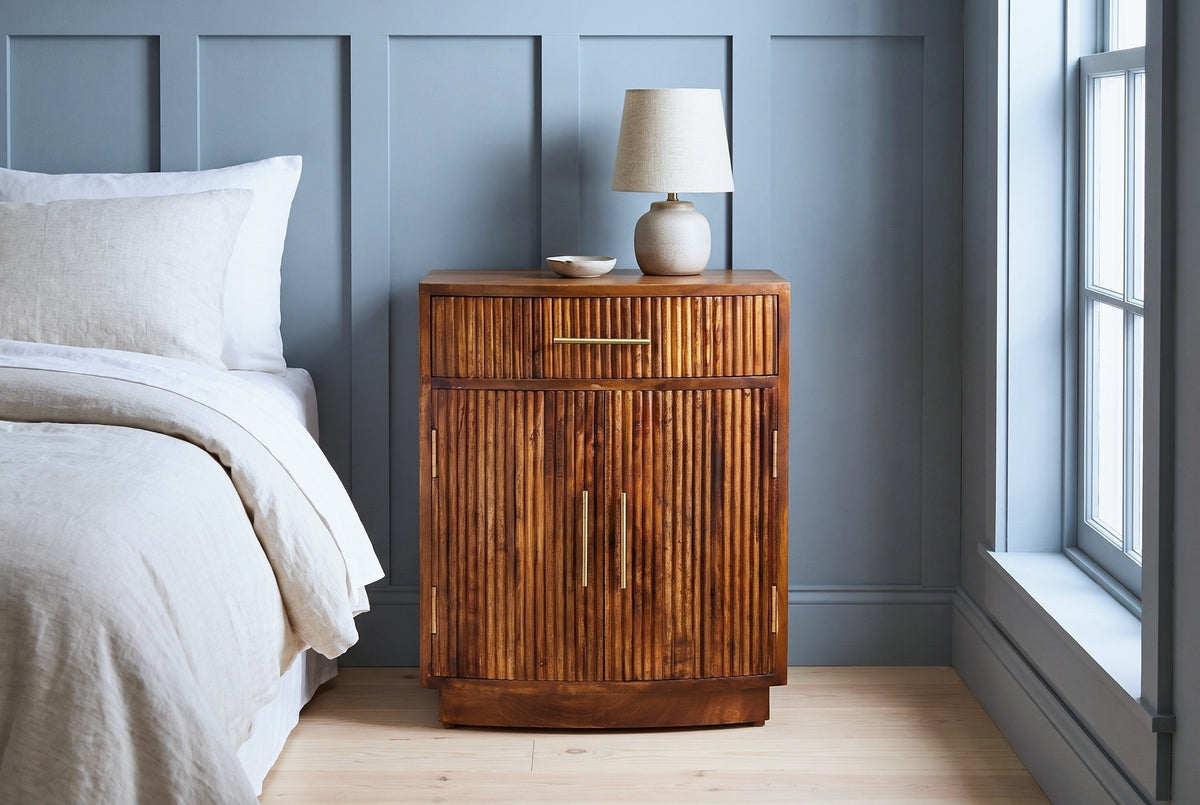 Gavoi fluted mango bow-front nightstand with a ceramic lamp in a Charleston bedroom with a blue-grey board-and-batten wall and pale heart-pine floors