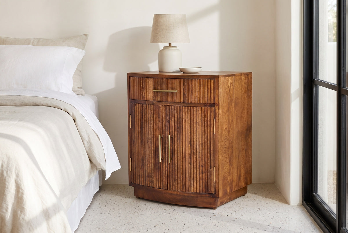 Gavoi fluted mango bow-front nightstand against a warm white lime plaster wall in a Scottsdale bedroom with a stone floor and a black steel window