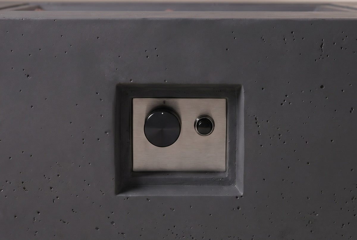 Close view of the Gela fire pit's control niche: a recessed niche in the concrete front face with a brushed steel plate, one control knob and one push button