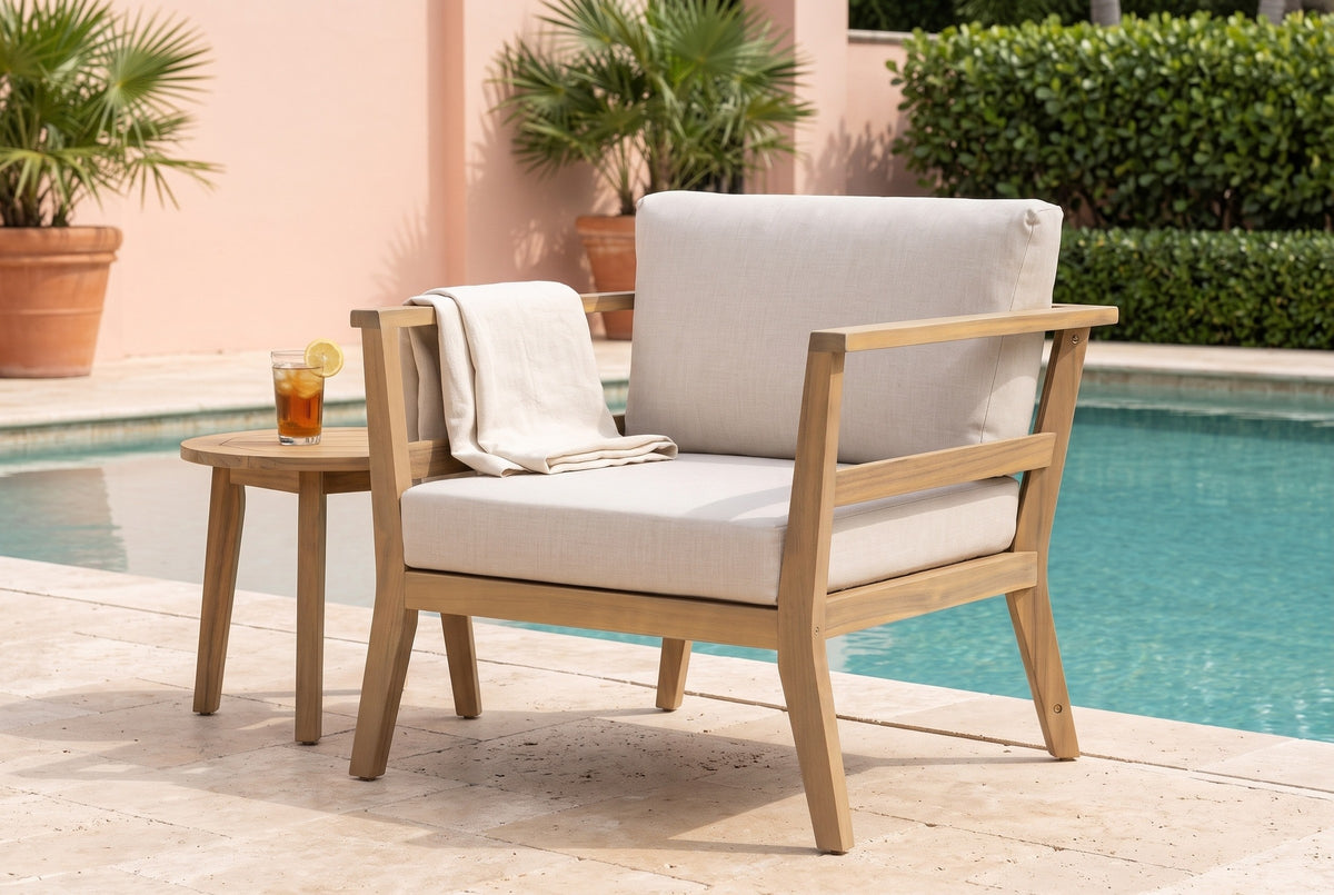 Geraci acacia club chair on a travertine pool terrace in Naples, Florida, with a coral stucco wall and potted palms (side table and throw not included)