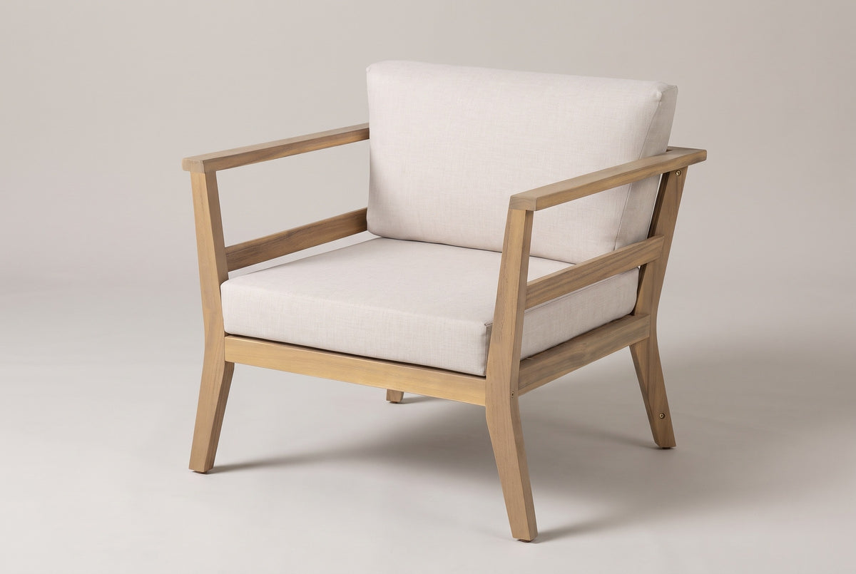 The Geraci acacia club chair with pale beige cushions, three-quarter view from the front on a light studio backdrop