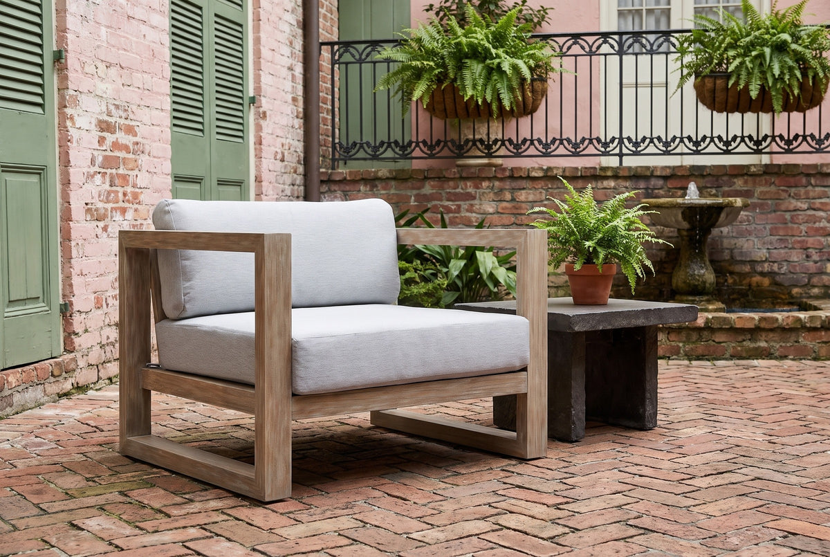 Giardini eucalyptus lounge chair in a New Orleans courtyard with a faded pink brick wall, green shutters, hanging ferns and a herringbone brick floor (side table not included)