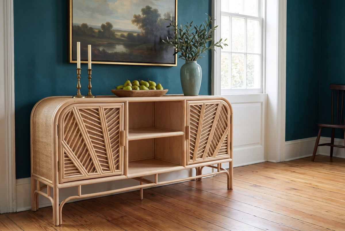 Giovinazzo rattan and cane sideboard against a deep peacock-teal wall in a Charleston dining room, with candlesticks, pears and a vase of olive branches on top