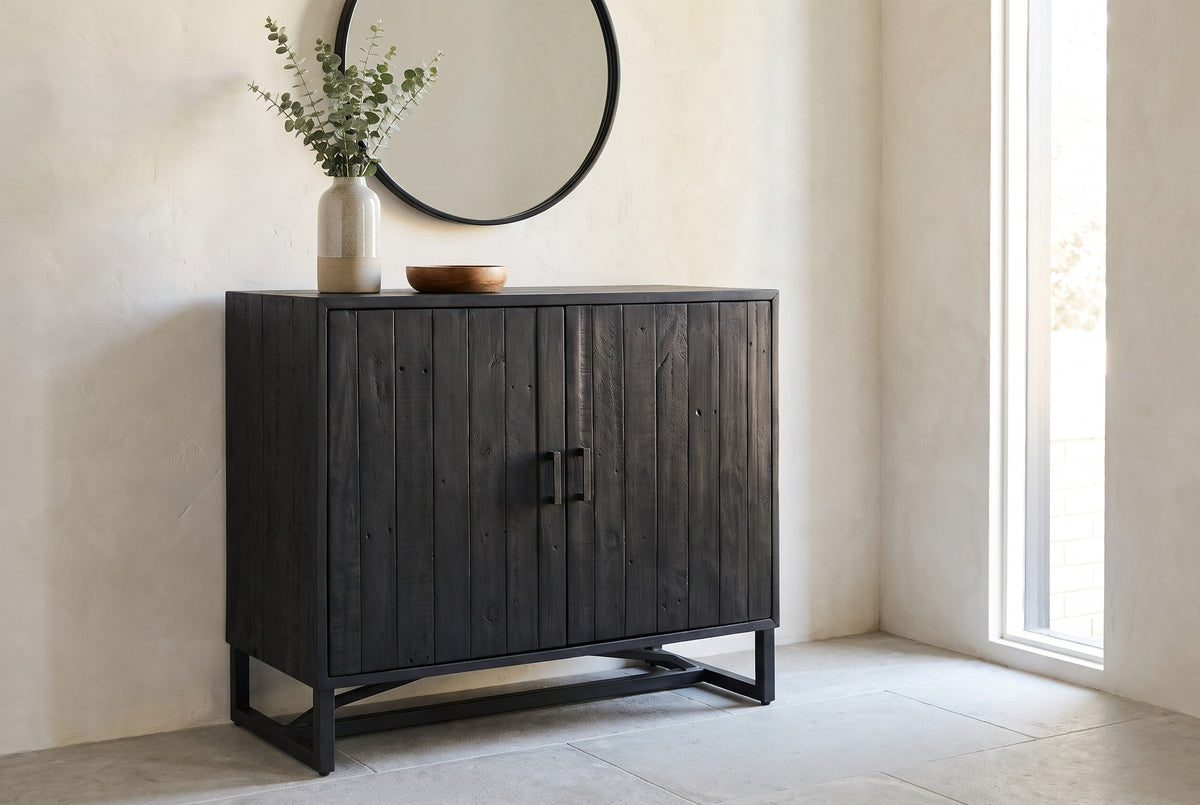 Gravina black reclaimed pine cabinet against a warm-white limewash wall in a Denver entryway, with a round black-framed mirror and eucalyptus in a vase
