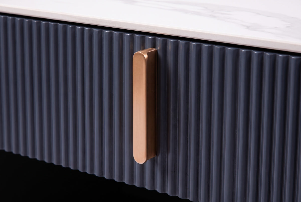 Close-up of the Guspini nightstand: the reeded charcoal drawer front, a gold-tone bar pull and the white stone top above it