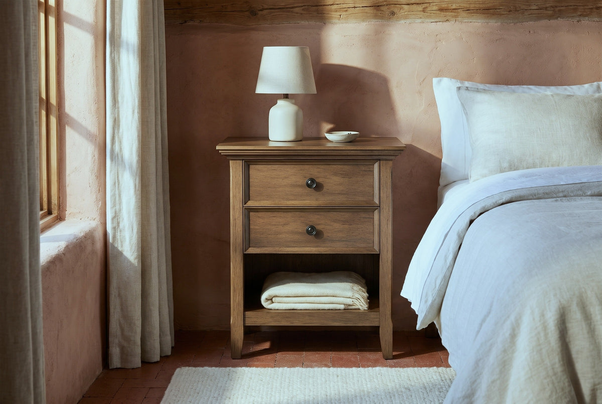Iglesias rustic brown nightstand with a ceramic lamp and a folded wool blanket in a Santa Fe adobe bedroom with a terracotta plaster wall and a brick tile floor