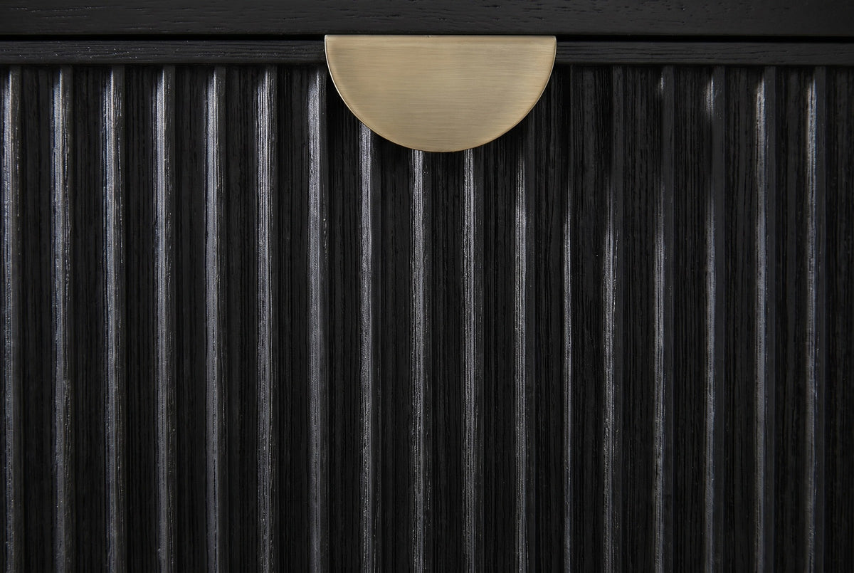 Close-up of the Isili nightstand: the fluted black drawer front with a half-moon pull in brushed antique brass