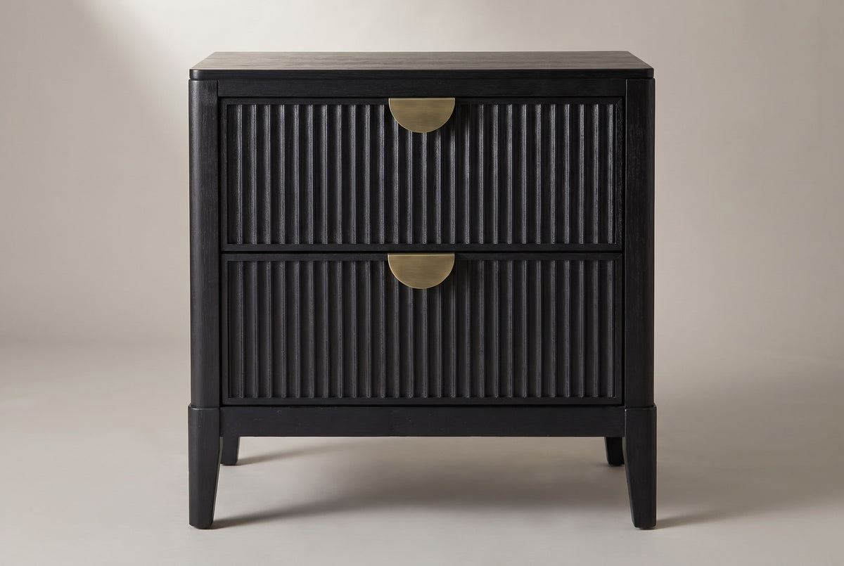 The Isili nightstand, front view on a light studio backdrop: two fluted drawers with brass half-moon pulls and four square tapered legs