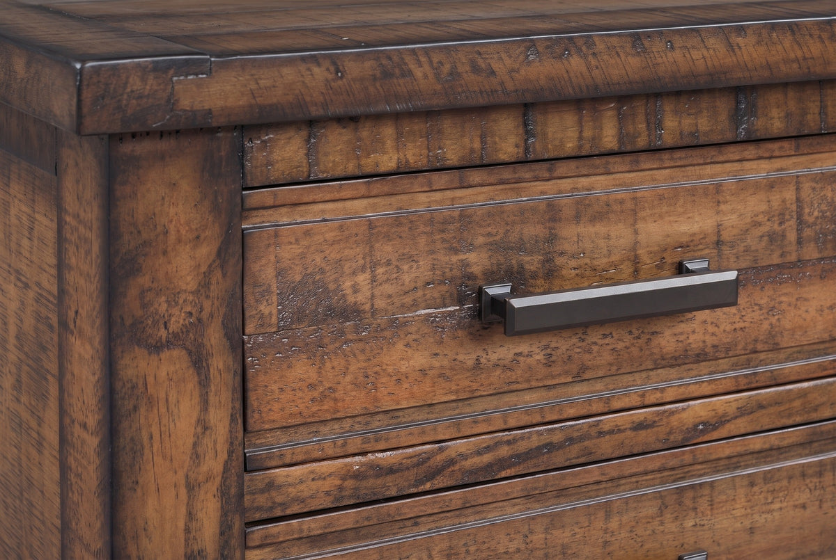 The corner of the framed top of the Ittiri nightstand with the wide front post, the top drawer front and one dark bronze bar pull on two small stepped posts