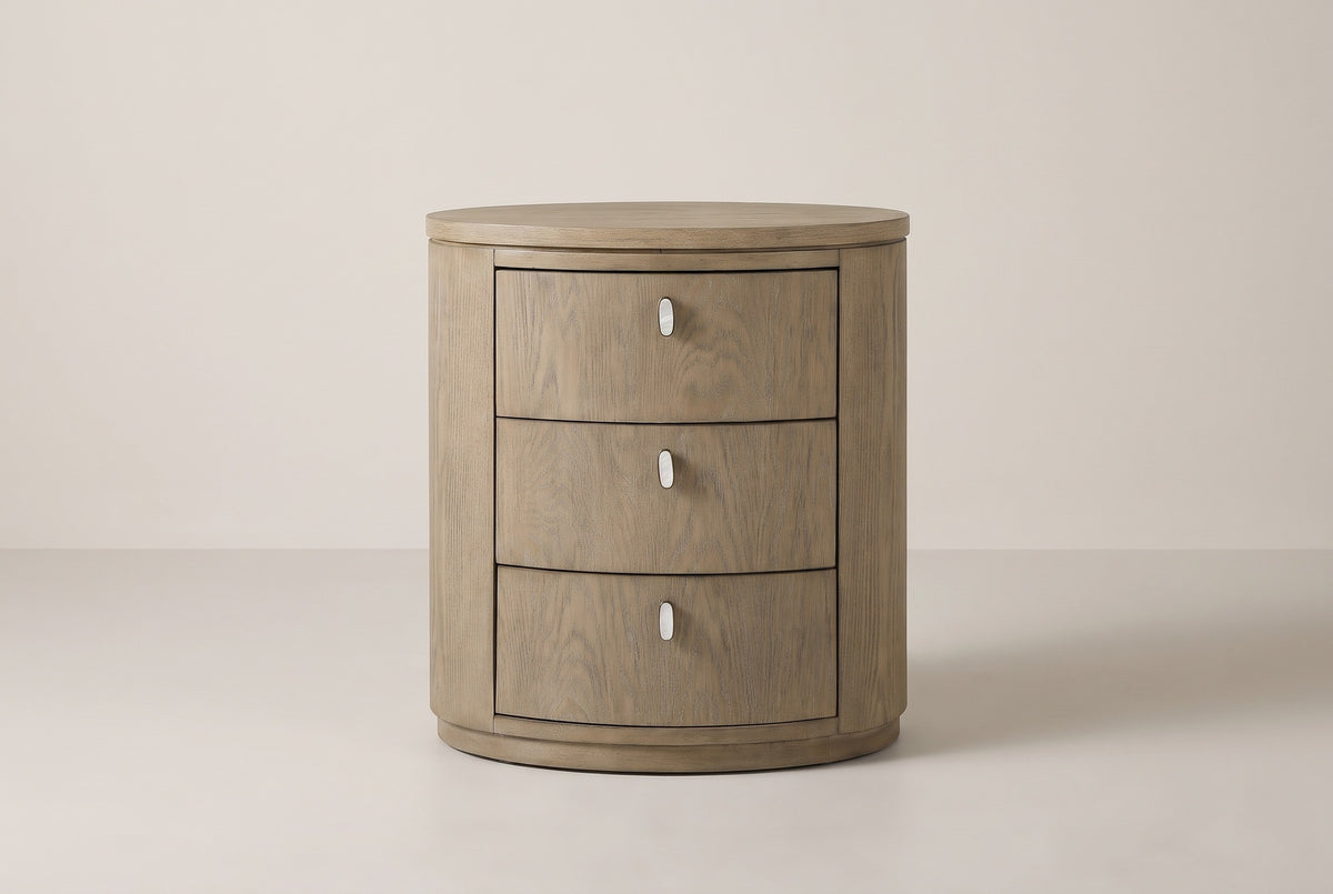 The Jerzu nightstand in cerused toffee, front view on a light studio backdrop: three bowed drawers with capsule pulls and a recessed oval plinth