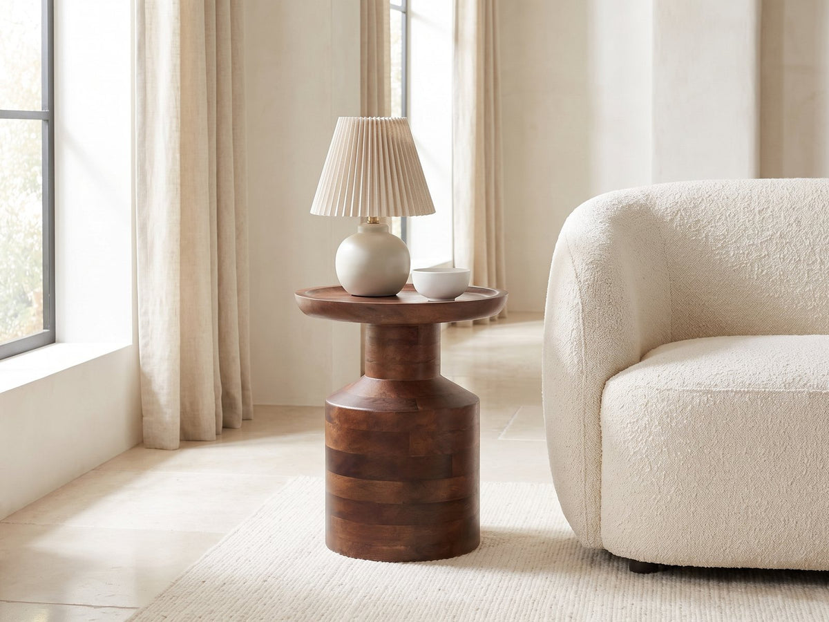Lagonegro Solid Mango Pedestal Side Table with a lamp and a ceramic bowl beside a cream boucle armchair in a bright plaster room
