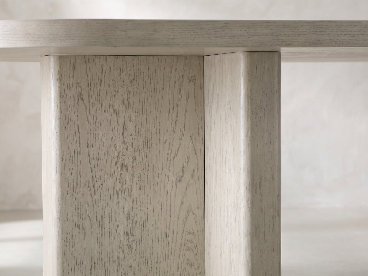 Close-up of the Laino 82-Inch Racetrack Oak Double Pedestal Dining Set with 4 Chairs: a T-shaped slab pedestal in grey-washed oak under the edge of the top