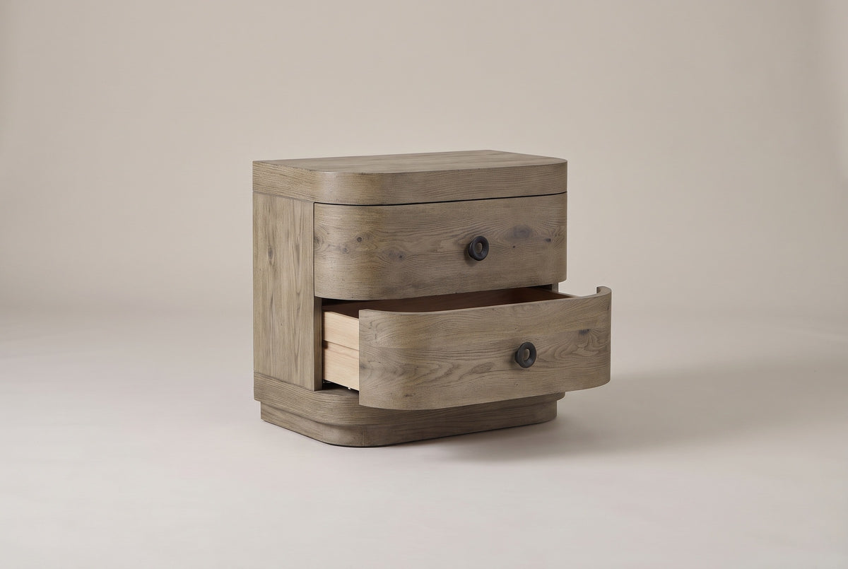 The Lanusei nightstand with its lower drawer pulled open, the drawer front with its black ring knob curving round the corner, and the upper drawer closed
