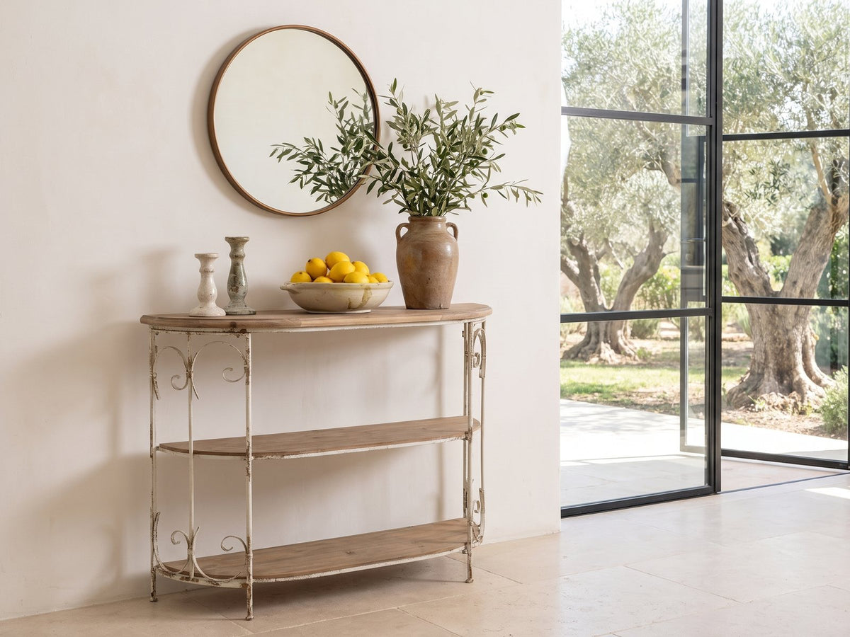 Latiano Fir and Scrolled Iron Three-Tier Console Table under a round bronze mirror beside a glass wall onto an olive garden in a sunlit villa