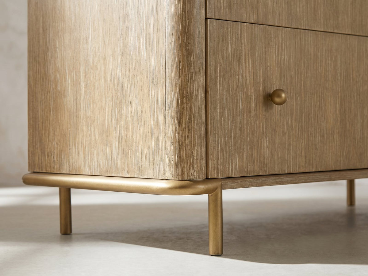 Close-up of the Lazise 38-Inch Sand Wash 5-Drawer Chest: the aged-brass metal sled under one end, the rod curving round the corner into a slim round leg