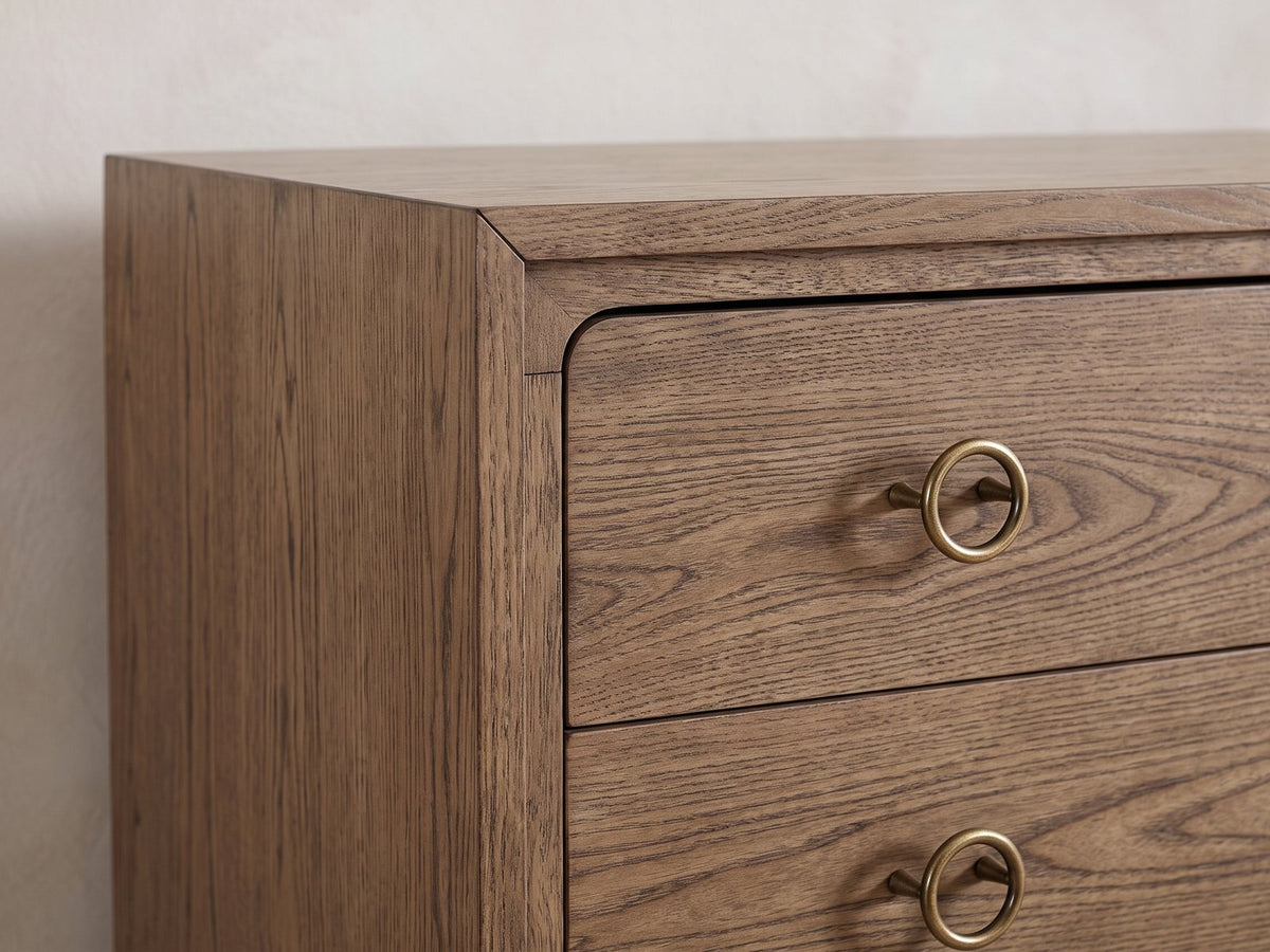 Close-up of the Legnago 40-Inch Latte Elm 5-Drawer Chest: an antique-brass ring pull, the rounded corner of the drawer stack and the mitred frame