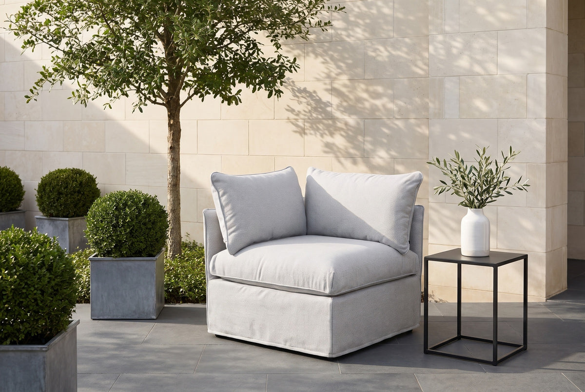 Lentini corner chair on charcoal pavers in a Dallas garden terrace, a cream limestone wall and boxwood planters behind (side table not included)